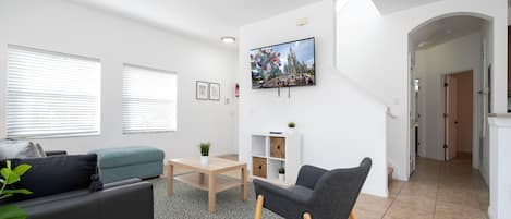 A modern living room with a sofa, a chair, a coffee table, and a TV mounted on the wall.