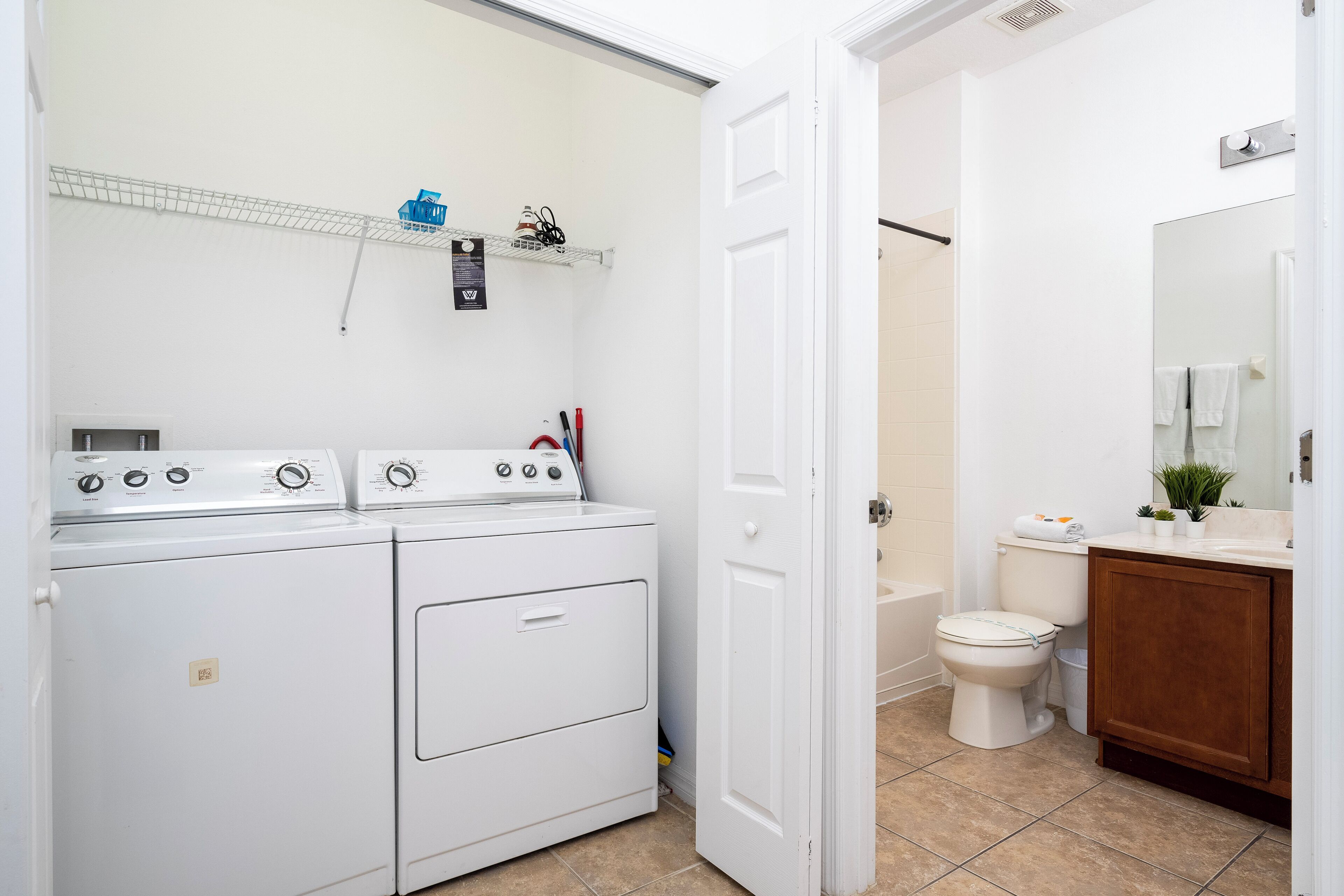 A laundry area with stacked washers and dryers, a white toilet, and a wooden cabinet in a bathroom.
