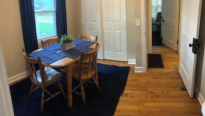 Uma área de refeições com uma mesa de madeira, quatro cadeiras, uma planta em vaso e um tapete azul.