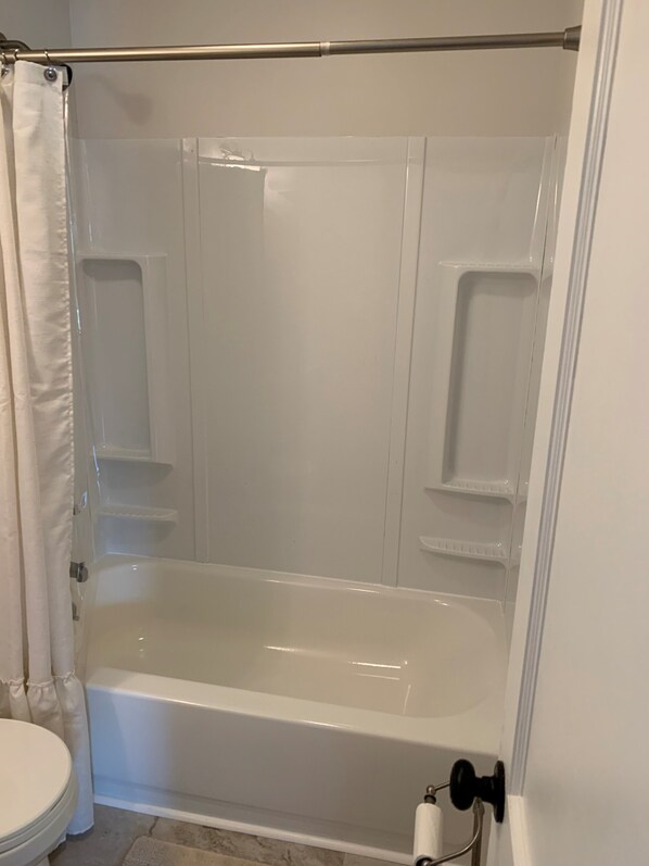 A bathroom with a bathtub, toilet, and shower curtain. - Historic Main Street Cottage (Troy)