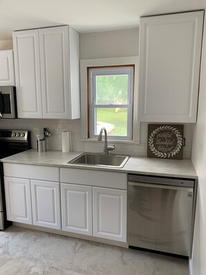 A modern kitchen with white cabinetry, a stainless steel sink, and a dishwasher. - Historic Main Street Cottage (Troy)