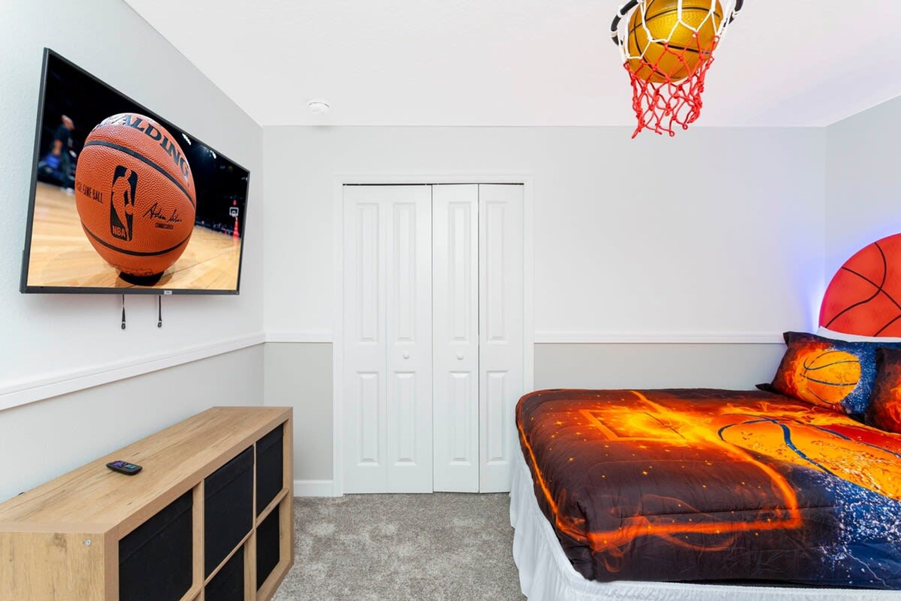 Quarto com cama, televisão, cesto de basquete e armário.