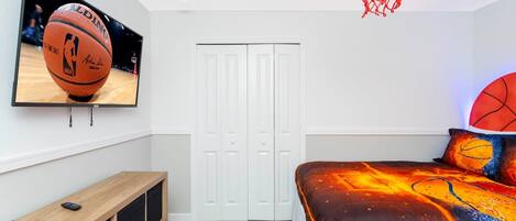 Quarto com cama, televisão, cesto de basquete e armário.