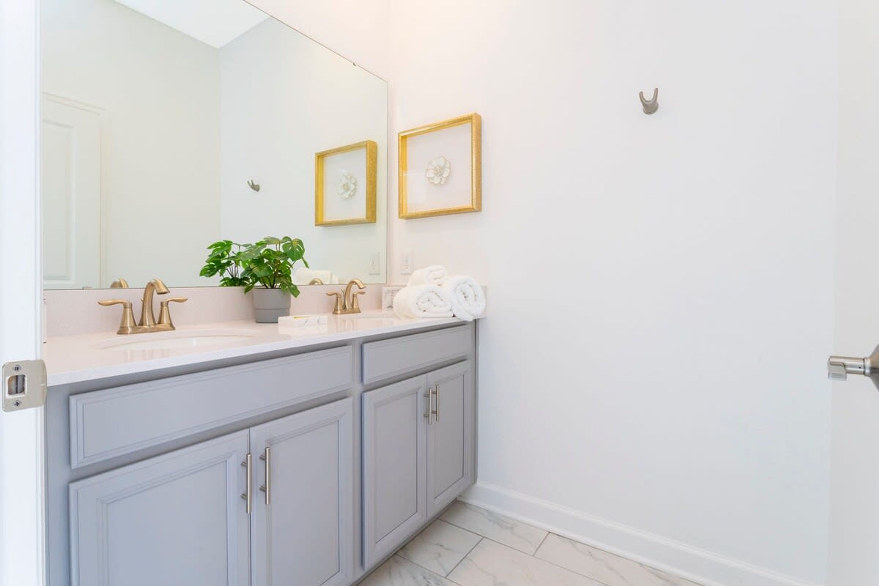 Un baño con un espejo grande, dos cuadros enmarcados con motivos florales, una planta en maceta y toallas ordenadas.