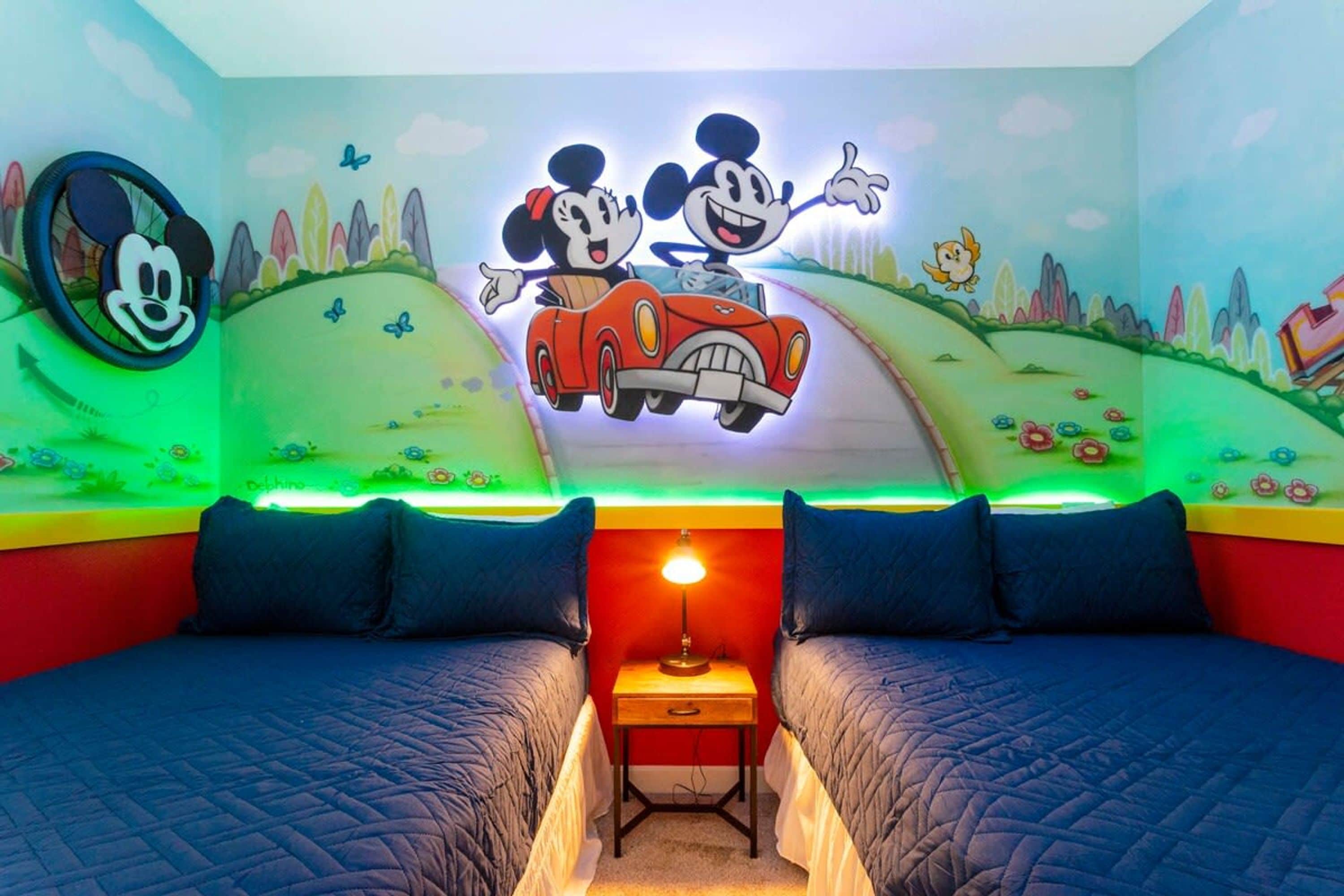 A children's room with two beds, a wall mural of Mickey and Minnie Mouse, and a nightstand with a lamp.