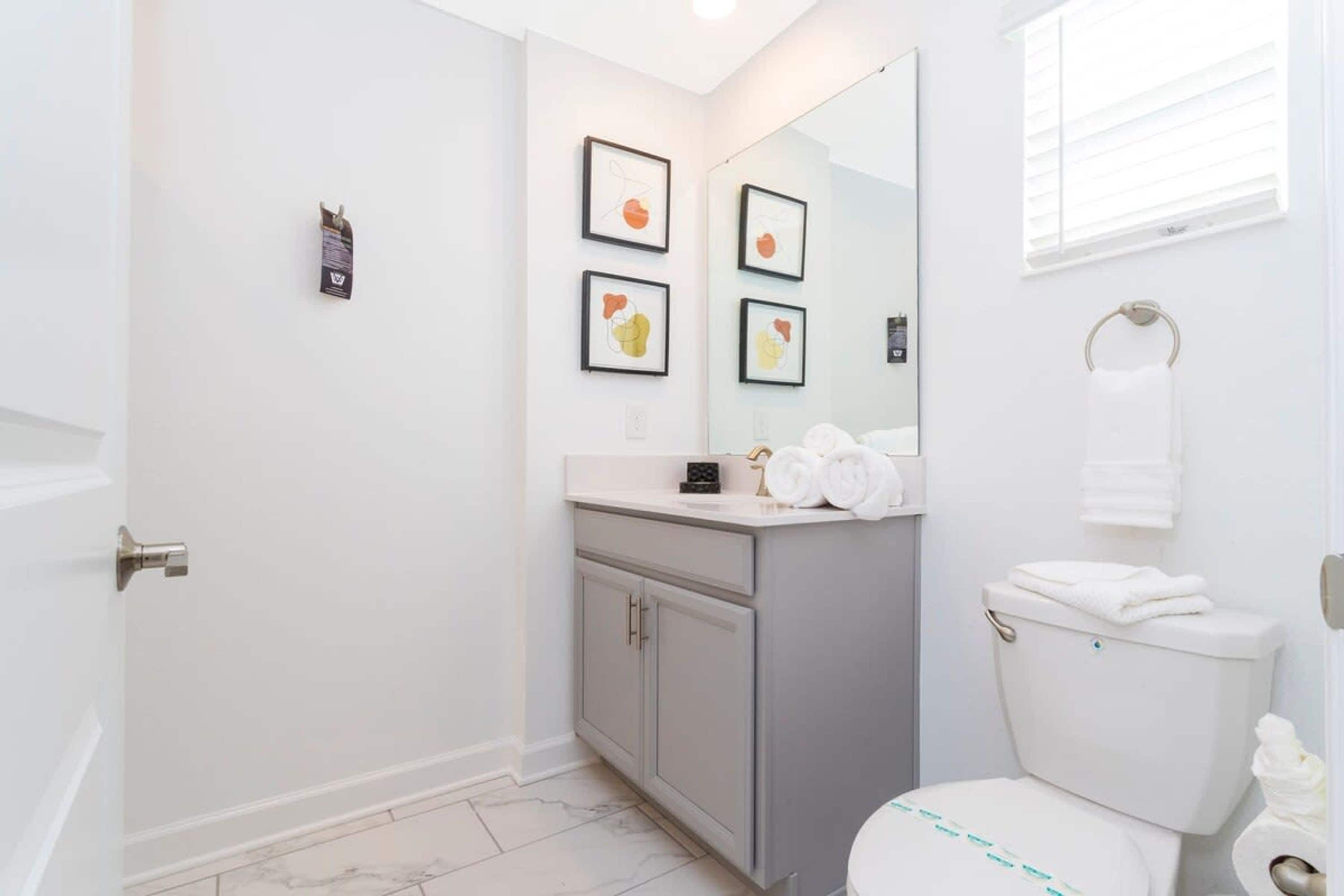 A modern bathroom with a white toilet, grey cabinets, and a countertop with towels.