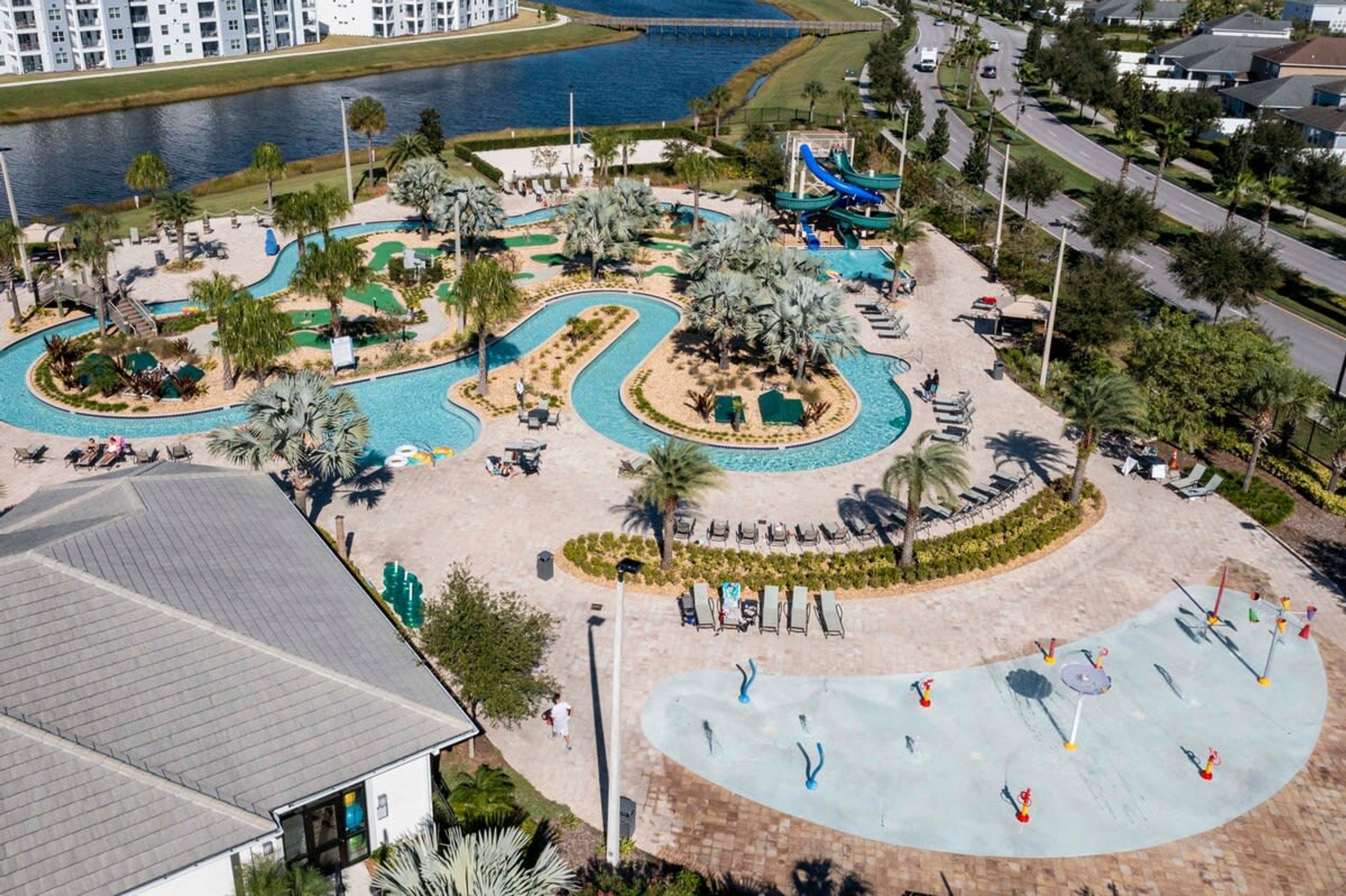 An aerial view of a resort with a central pool area, palm trees, and a water slide.