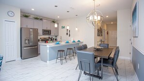 A modern kitchen with a central island, stainless steel appliances, and a dining area with a marble floor. - Wonderful 5 Bedroom w Pool Close to Disney 4801 (Kissimmee)