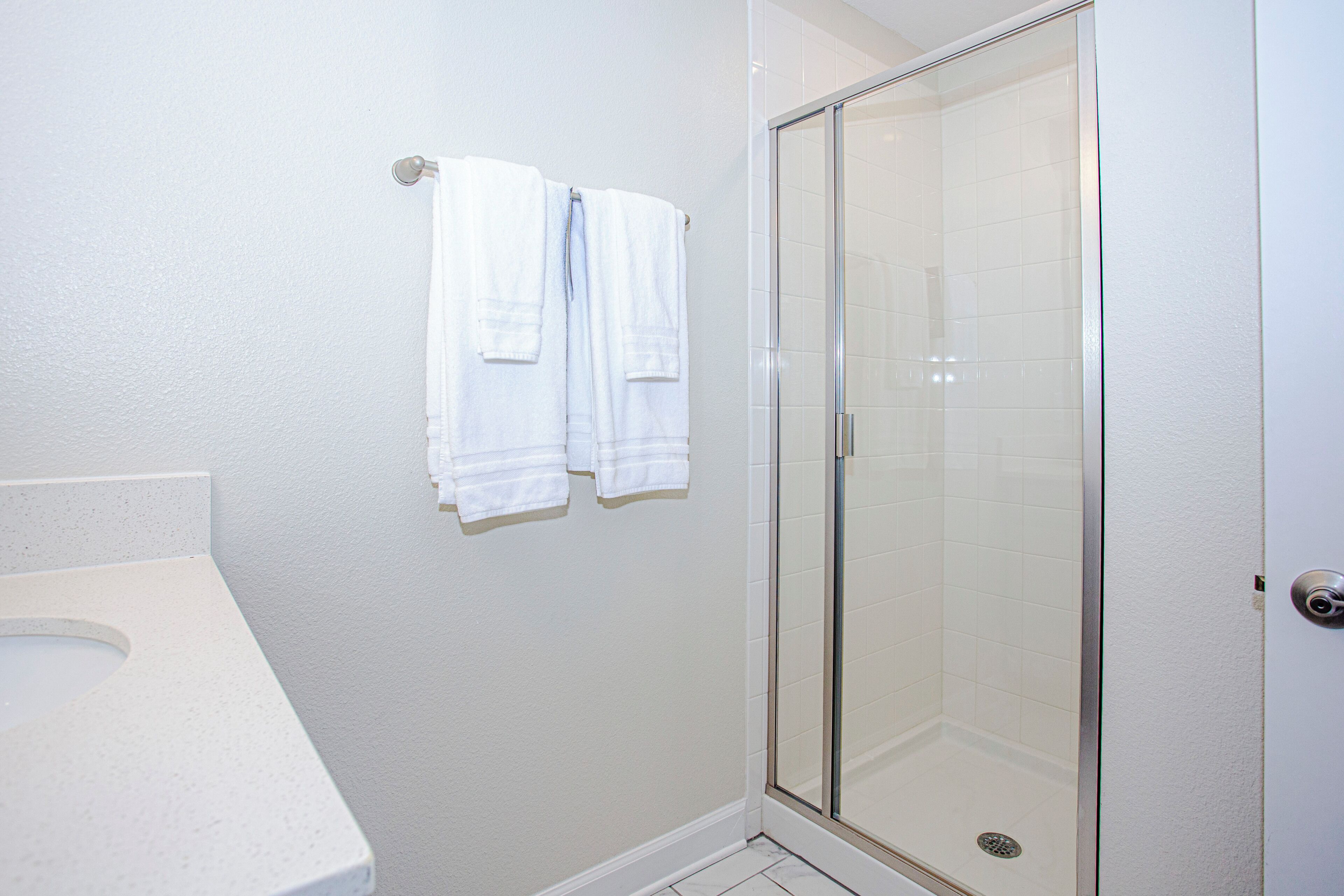 Un baño con inodoro, cabina de ducha de vidrio y dos toallas blancas colgadas en un perchero.