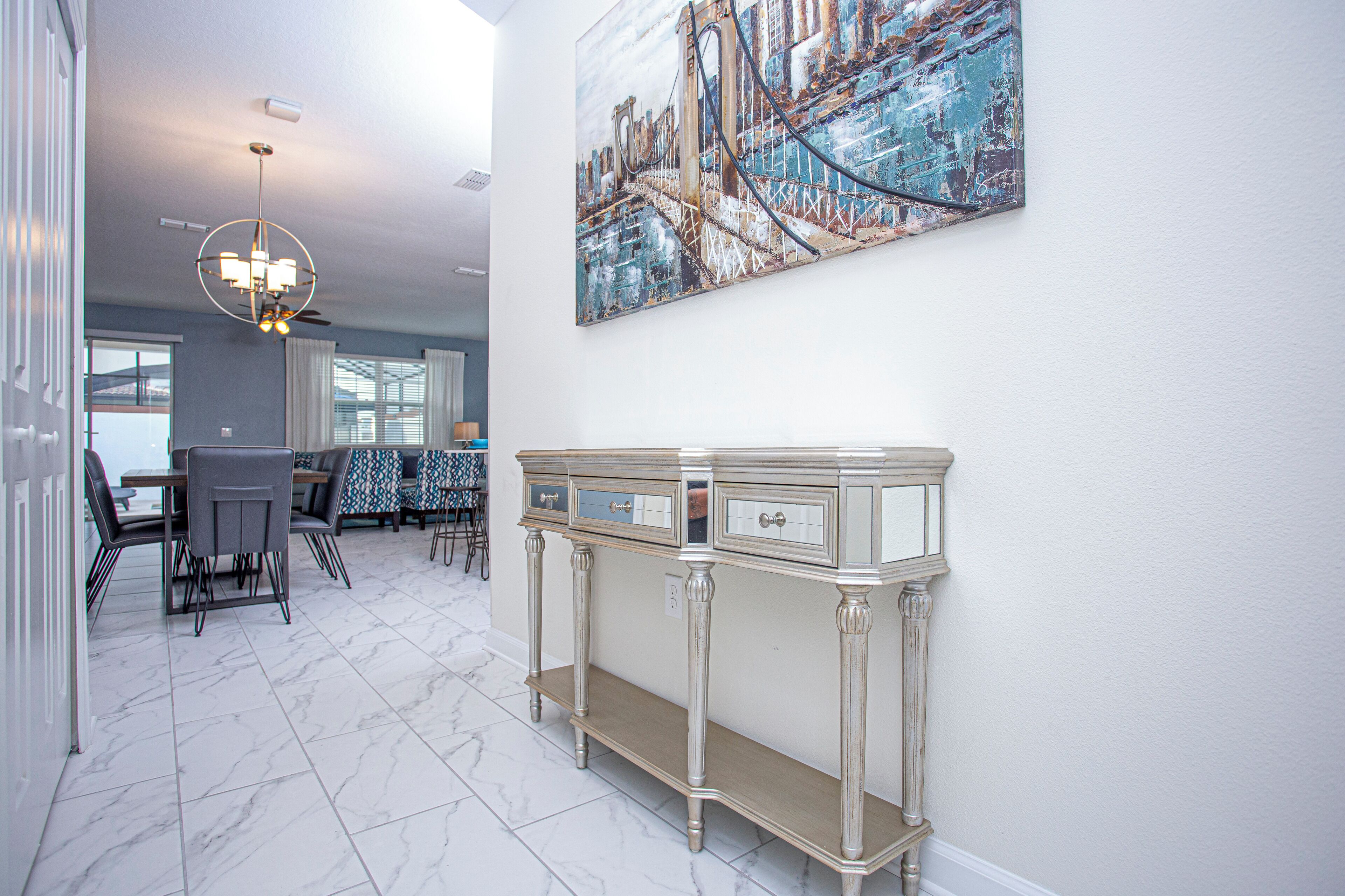 Uma sala de jantar com piso de mármore, um console branco e um quadro de uma ponte na parede.