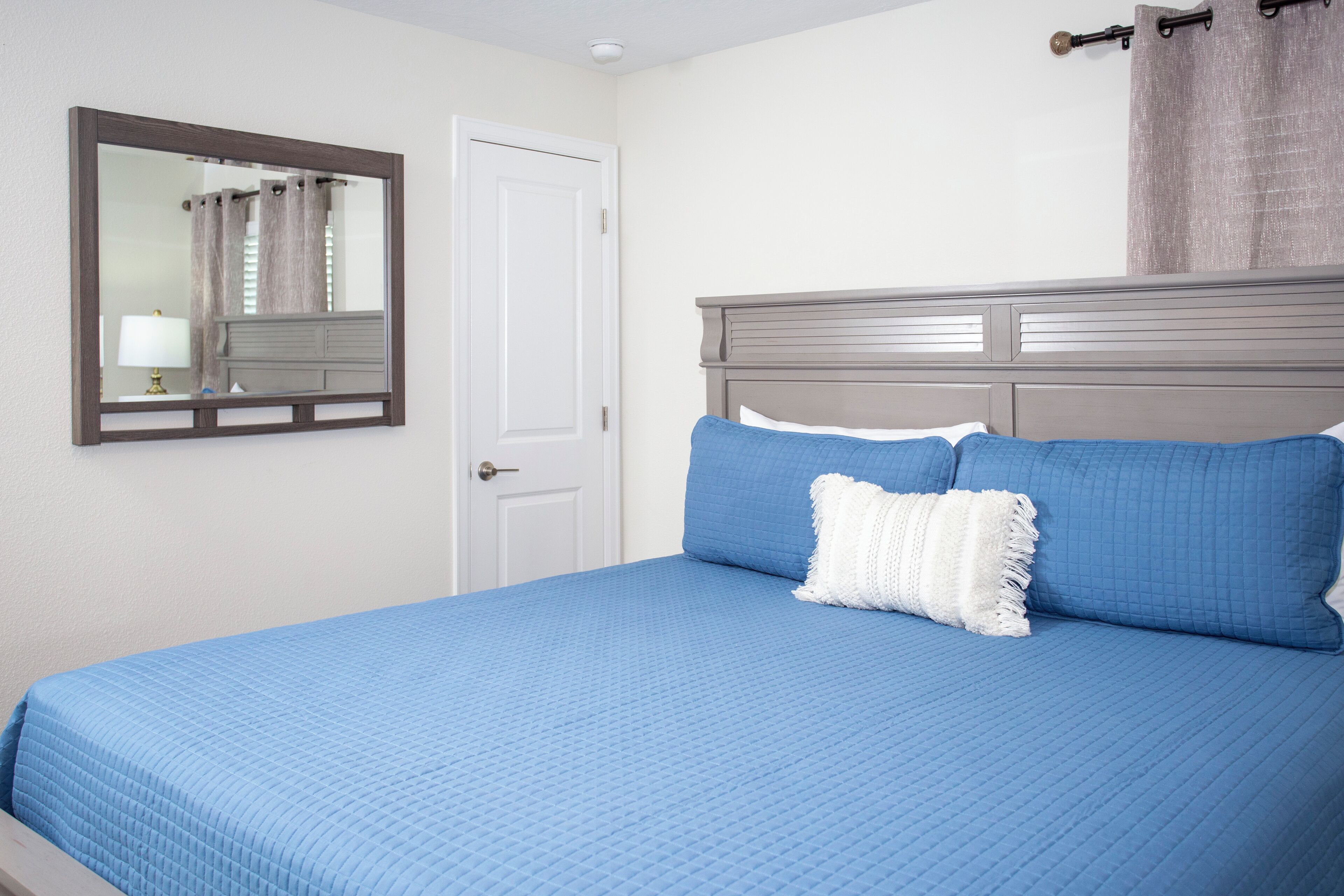 A bedroom with a bed, a nightstand, a mirror, and a door.