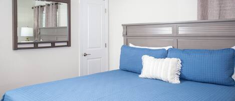 A bedroom with a bed, a nightstand, a mirror, and a door.
