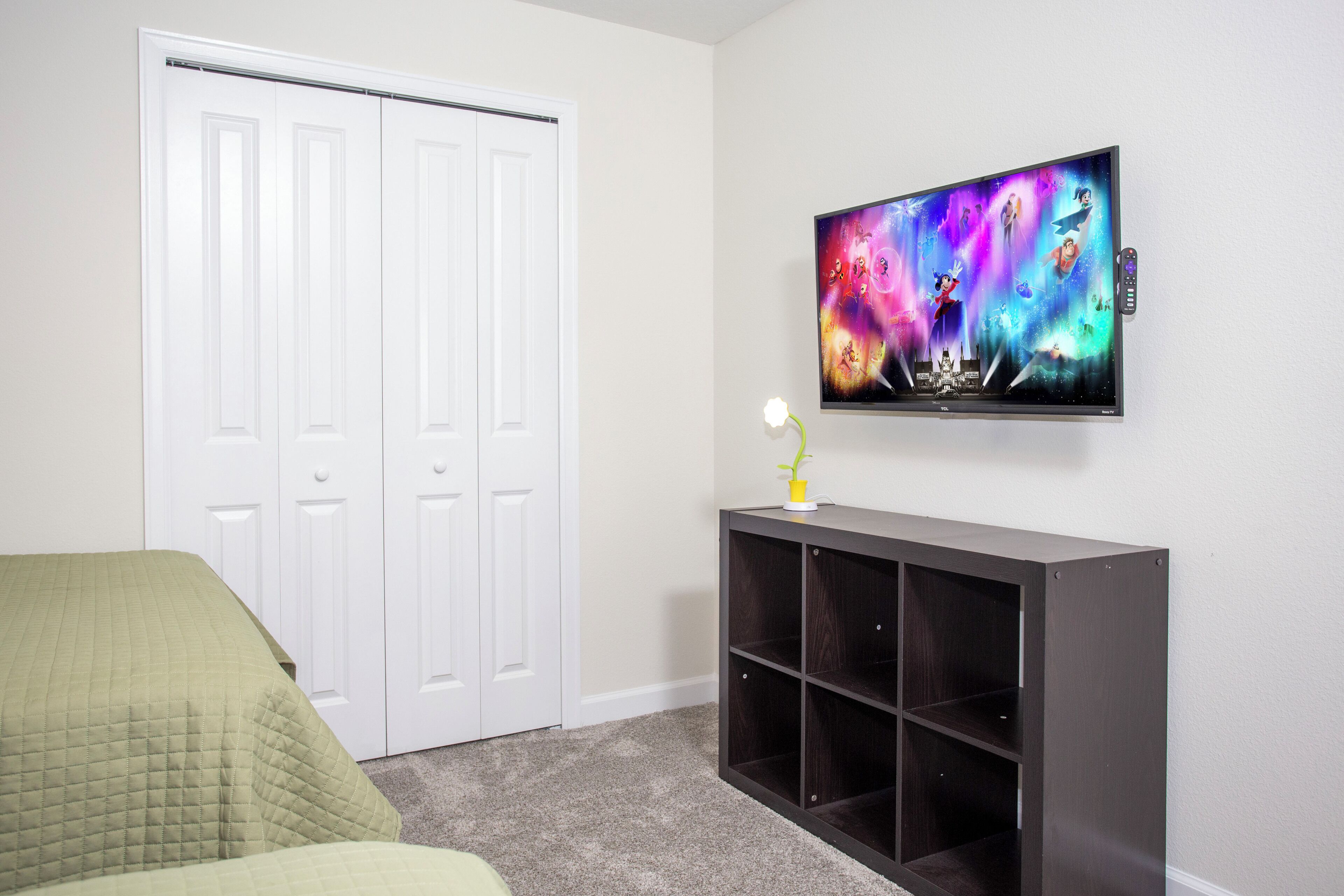 A bedroom with a bed, a TV mounted on the wall, a white closet, and a dark wooden console table.