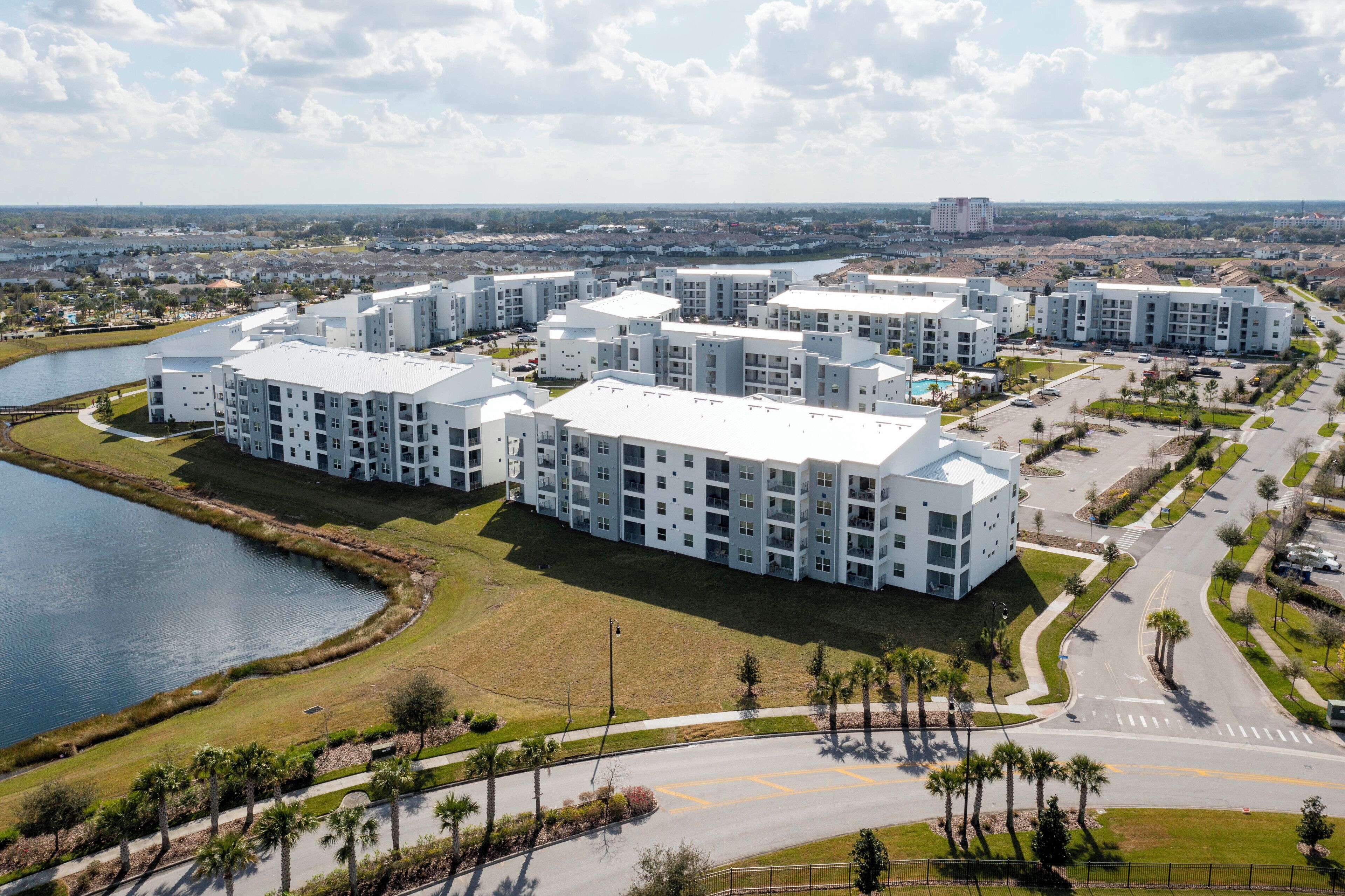 A modern apartment complex with multiple buildings, a central courtyard, and a body of water.