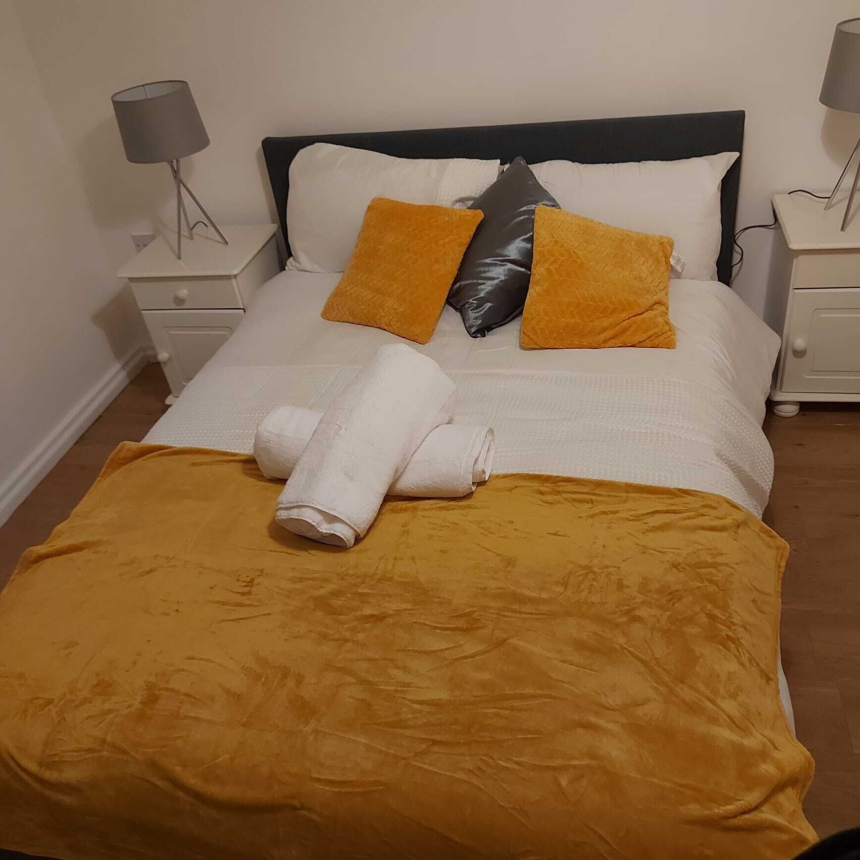 A neatly made bed with a white and yellow bedspread, two pillows, and a folded towel.