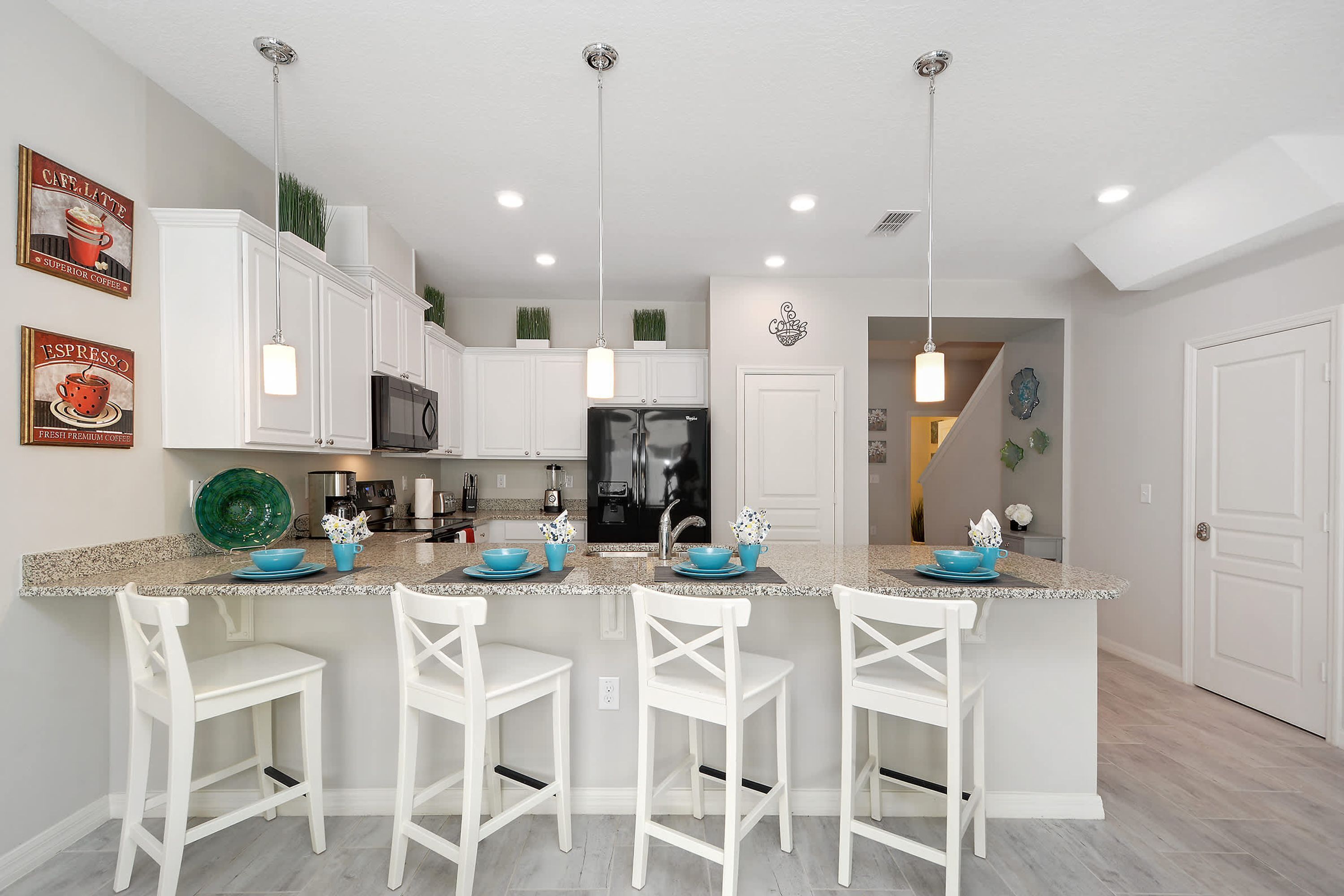 A kitchen with white cabinets, a central island with bar stools, and pendant lighting.