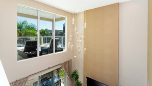 A modern living room with a large window, a flat-screen TV, and a ceiling light fixture. - Marvelous 4 Bd Close to Disney Magic Village 3153 (Kissimmee)