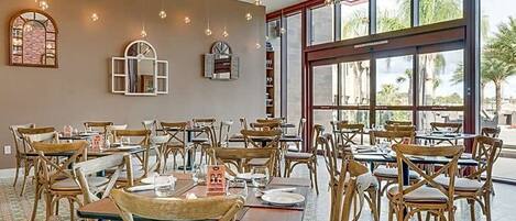 Un restaurant avec des tables et des chaises en bois, de grandes fenêtres et des lampes suspendues.