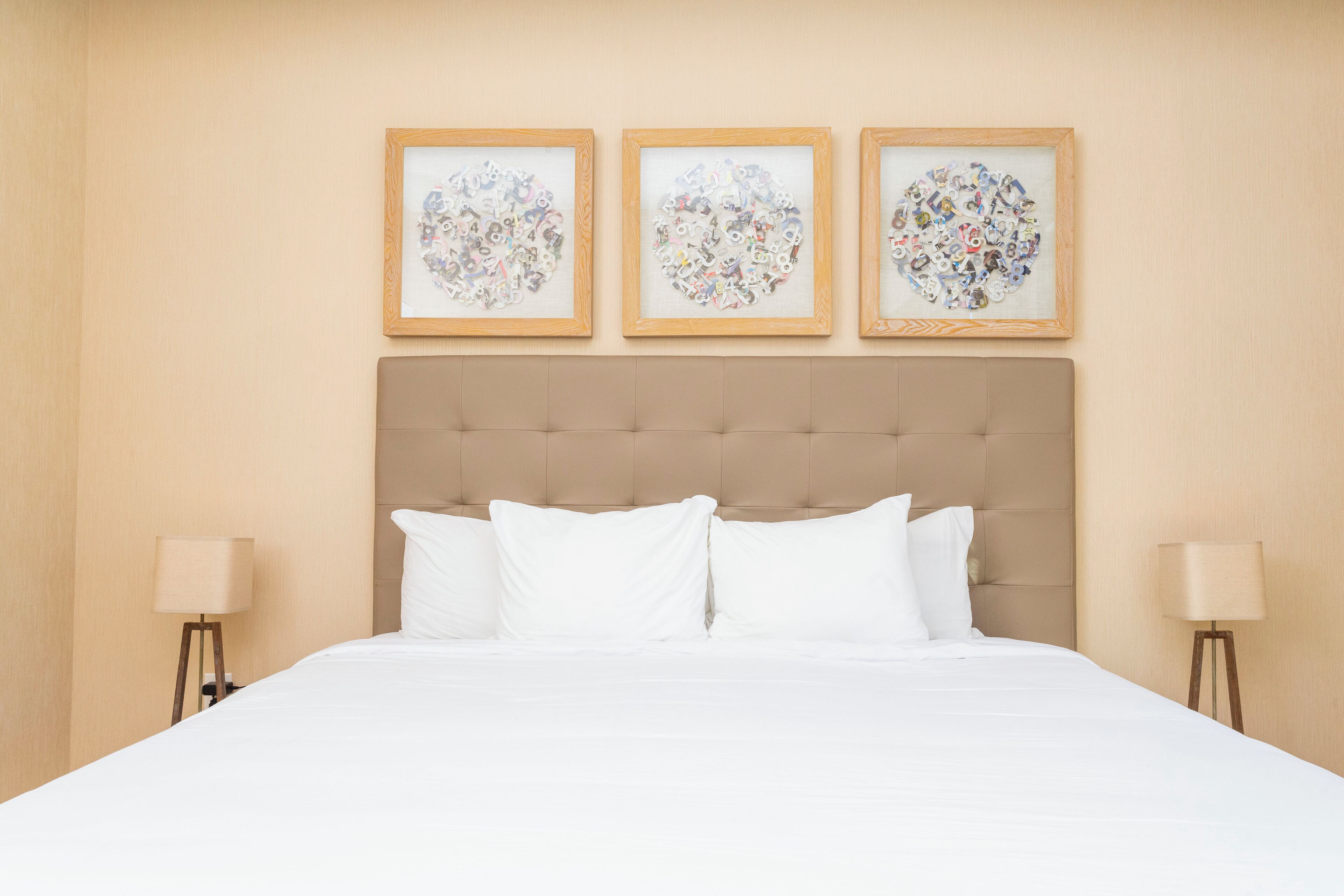 A neatly made bed with white linens, a tufted headboard, and three framed artworks above it.