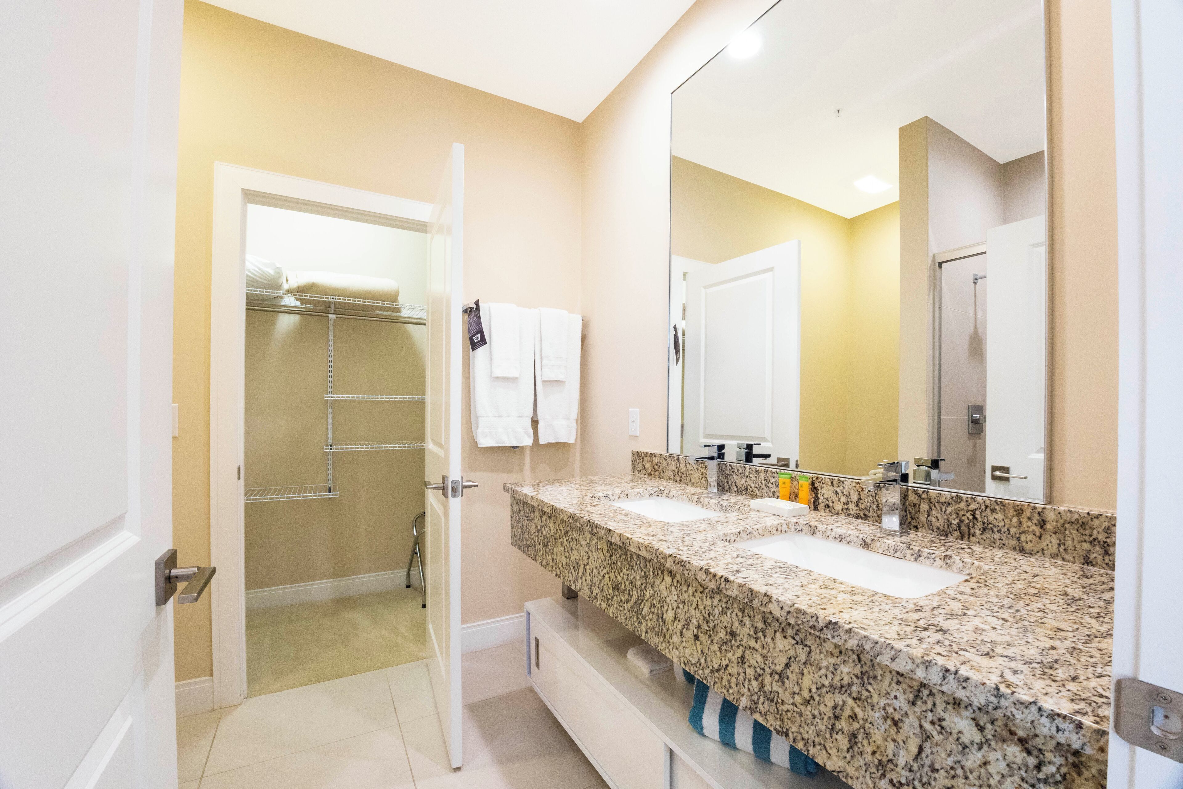 Un baño con lavamanos doble, un espejo grande y un vestidor.