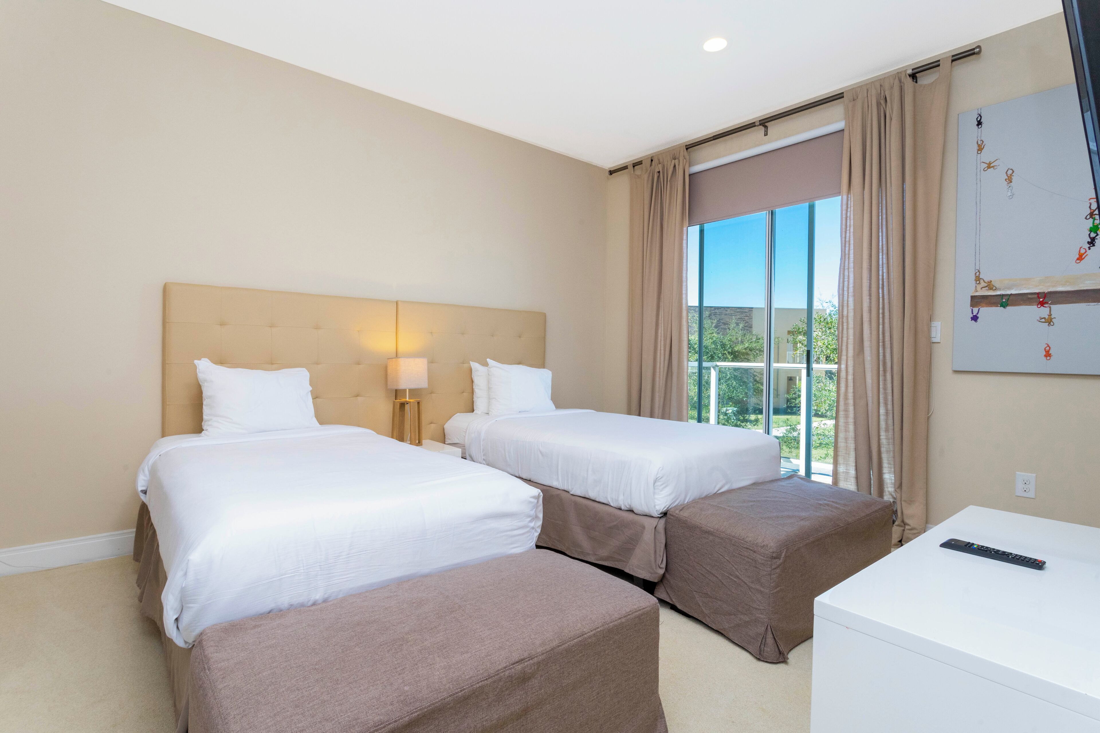 A hotel room with two beds, a desk, and a large window with curtains.