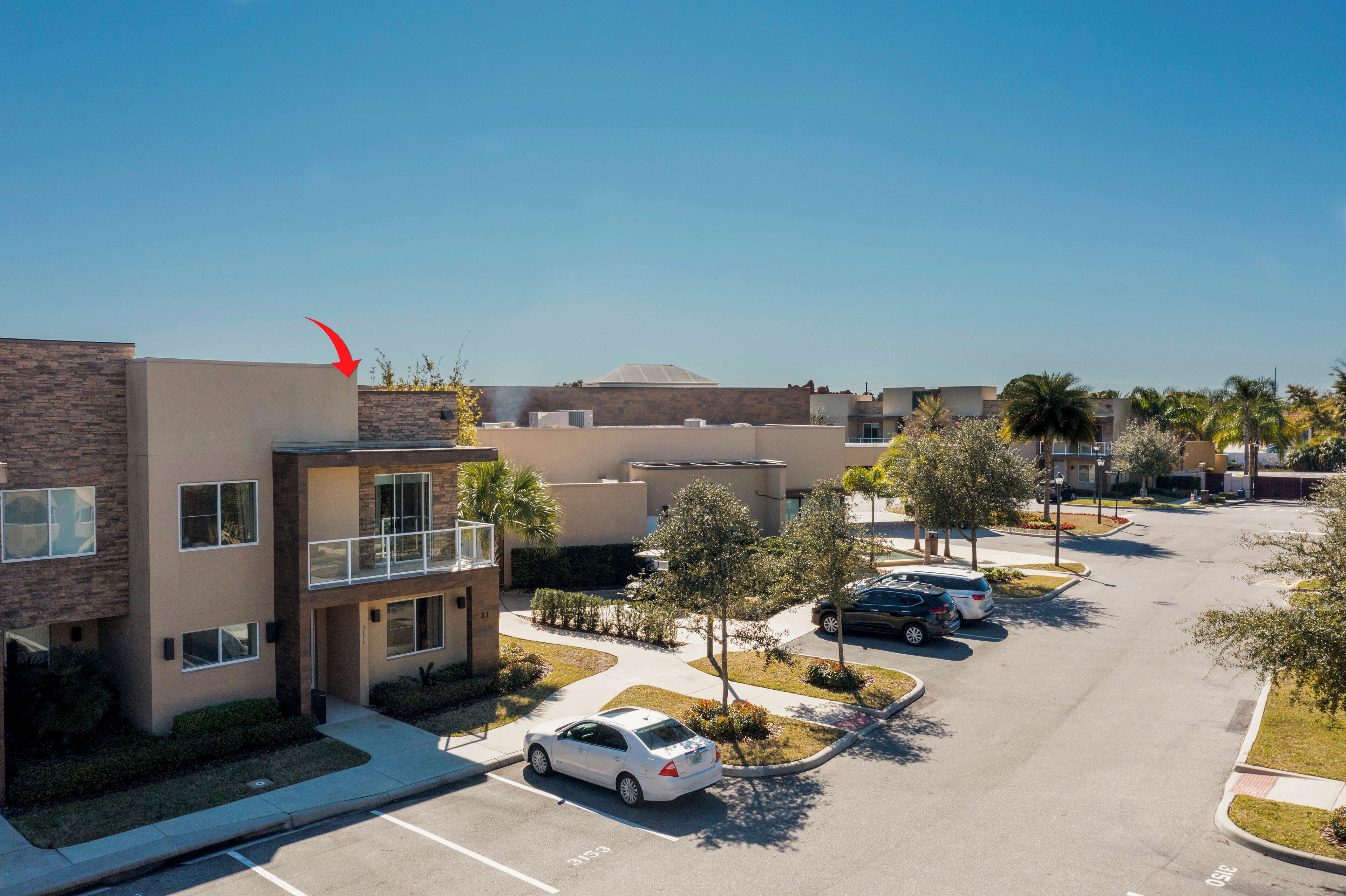 A multi-story building with a parking lot, surrounded by trees and a clear sky.