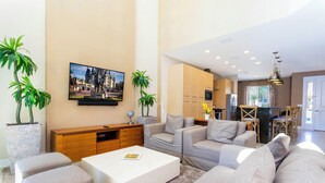 A modern living room with a white coffee table, grey sofas, and a large flat-screen TV mounted on the wall. - Marvelous 4 Bd Close to Disney Magic Village 3153 (Kissimmee)