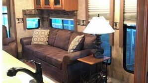 A compact RV interior with a kitchenette, a sofa, and a table with a lamp. - Lake Fork bass fishing (Quitman)