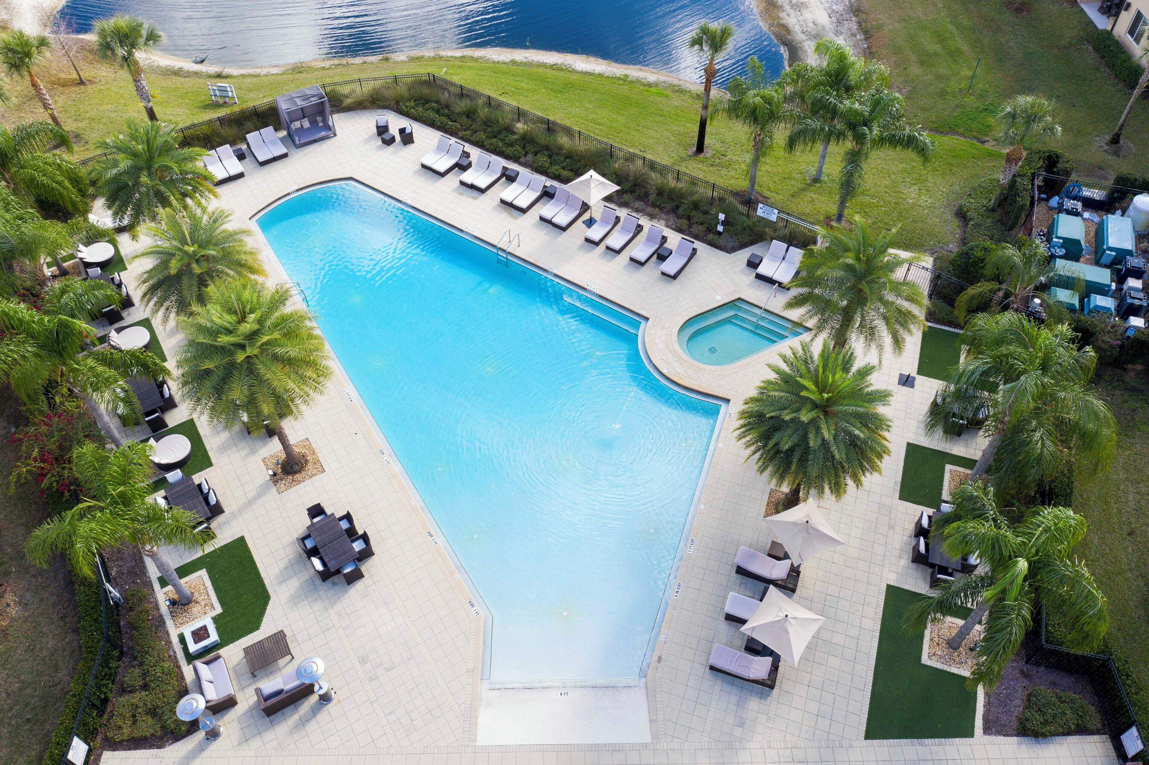 An aerial view of a resort pool area with sun loungers, palm trees, and a clear blue pool.