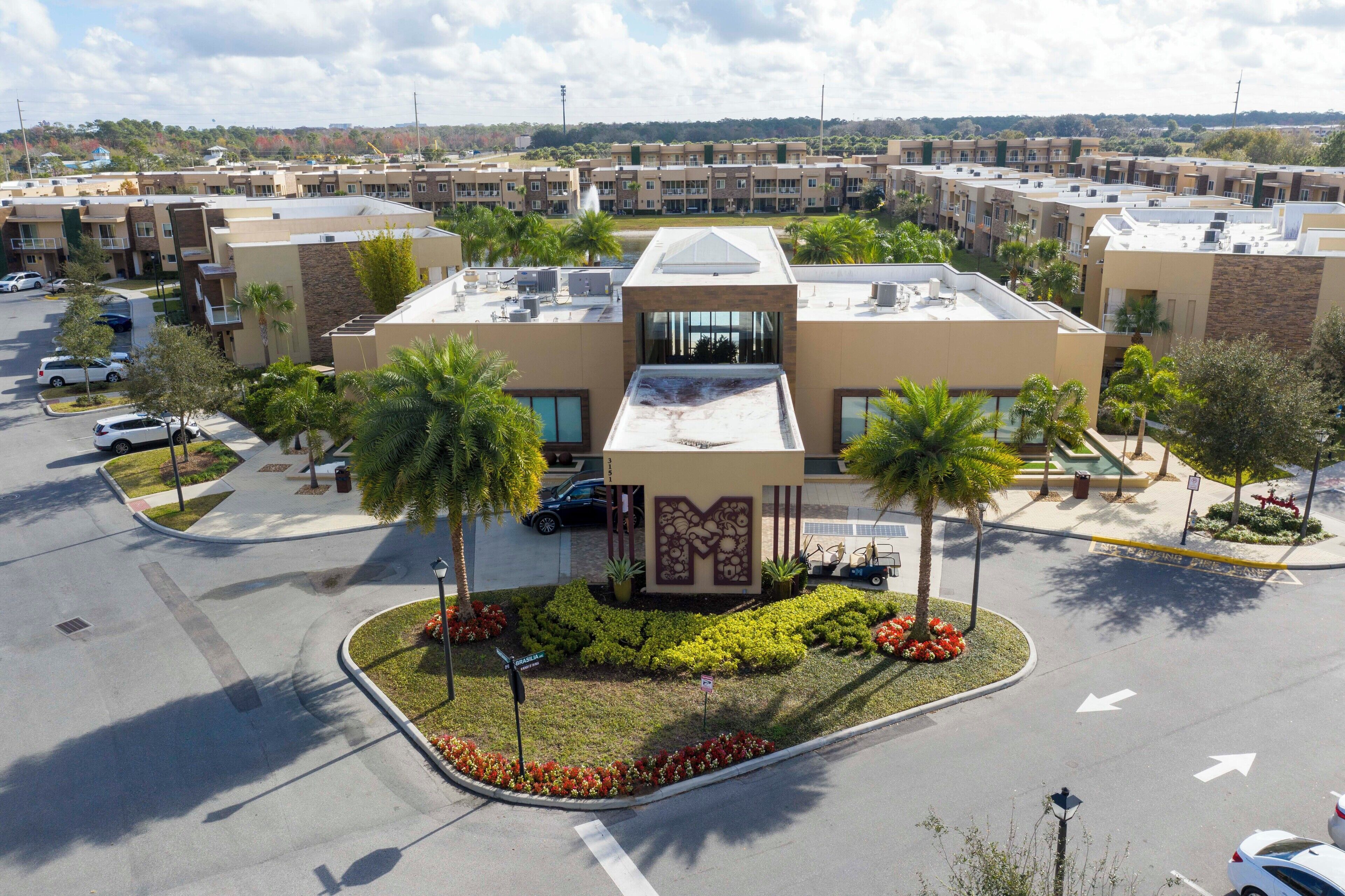 A multi-story hotel with a central courtyard, parking lot, and surrounding greenery.
