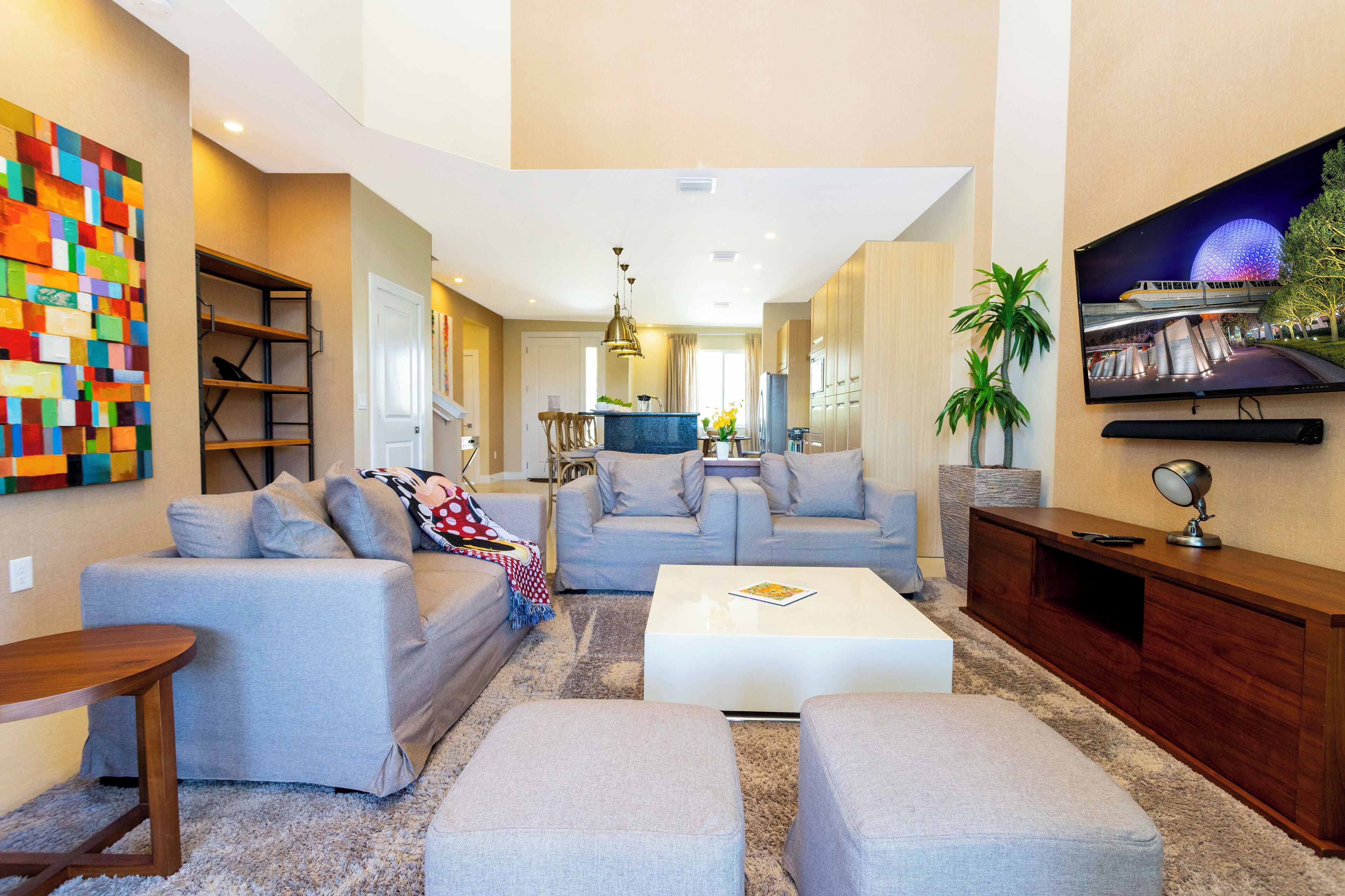 A modern living room with a sofa set, a coffee table, a TV mounted on the wall, and a colorful abstract painting on the wall.