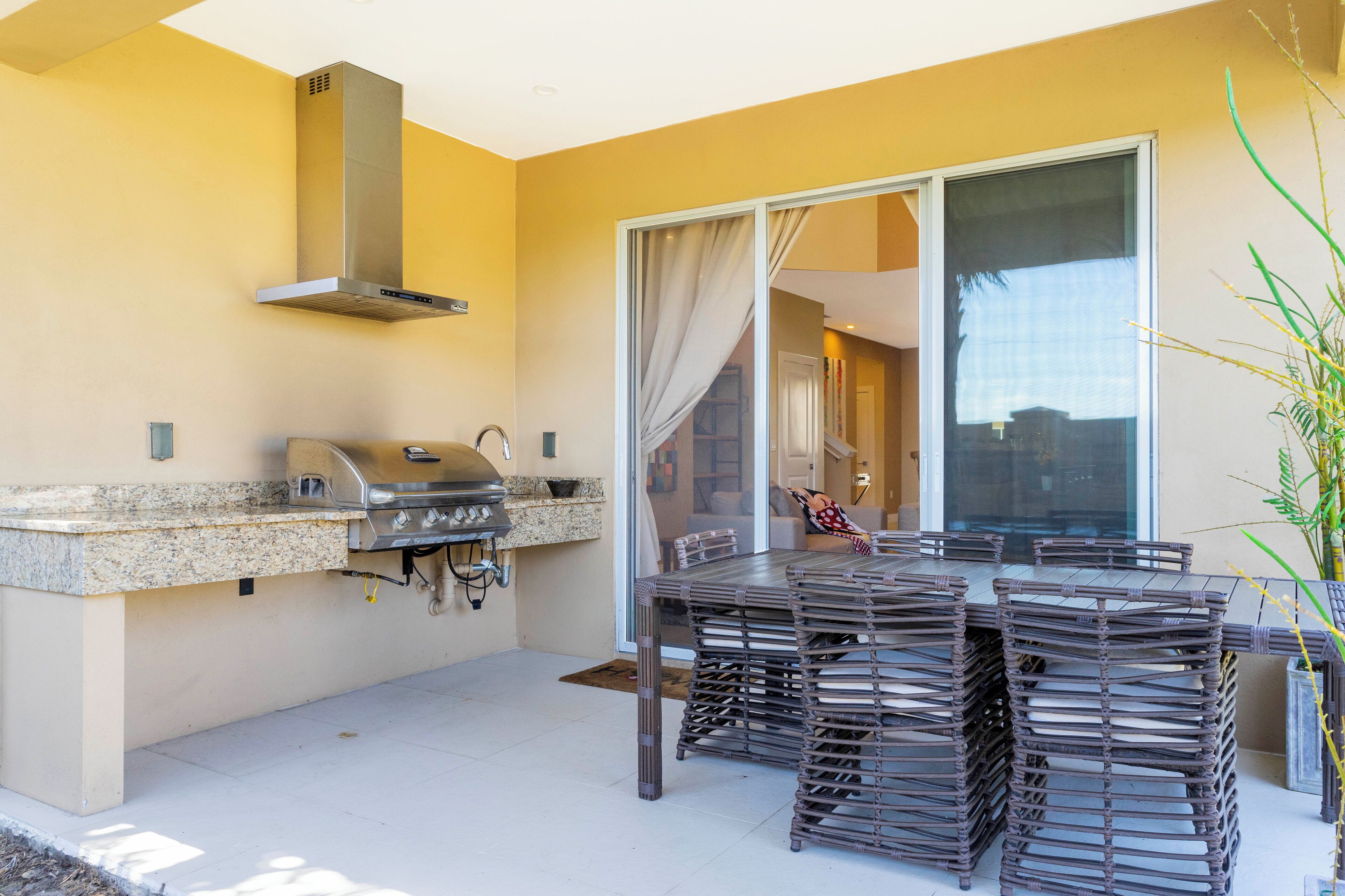 An outdoor kitchen with a grill, a dining table with chairs, and a sliding glass door leading to an interior space.