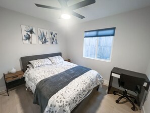 A bedroom with a bed, a desk, and a window.