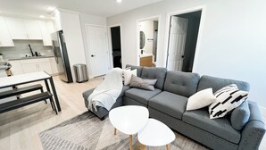 Un salon moderne avec un canapé gris, deux petites tables rondes blanches et un tapis gris à motifs.