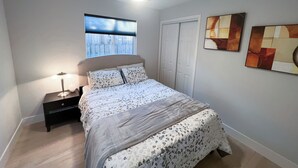 Une chambre à coucher comprenant un lit, une table de chevet, un ventilateur de plafond, une fenêtre avec des stores et deux œuvres d’art murales.