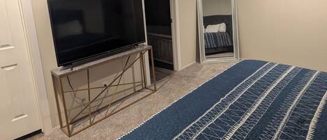 A bedroom with a bed, a television on a stand, a ceiling fan, and a door leading to a closet.