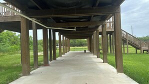 Un passeig de formigó sota una estructura de fusta amb baranes, envoltat de vegetació.
