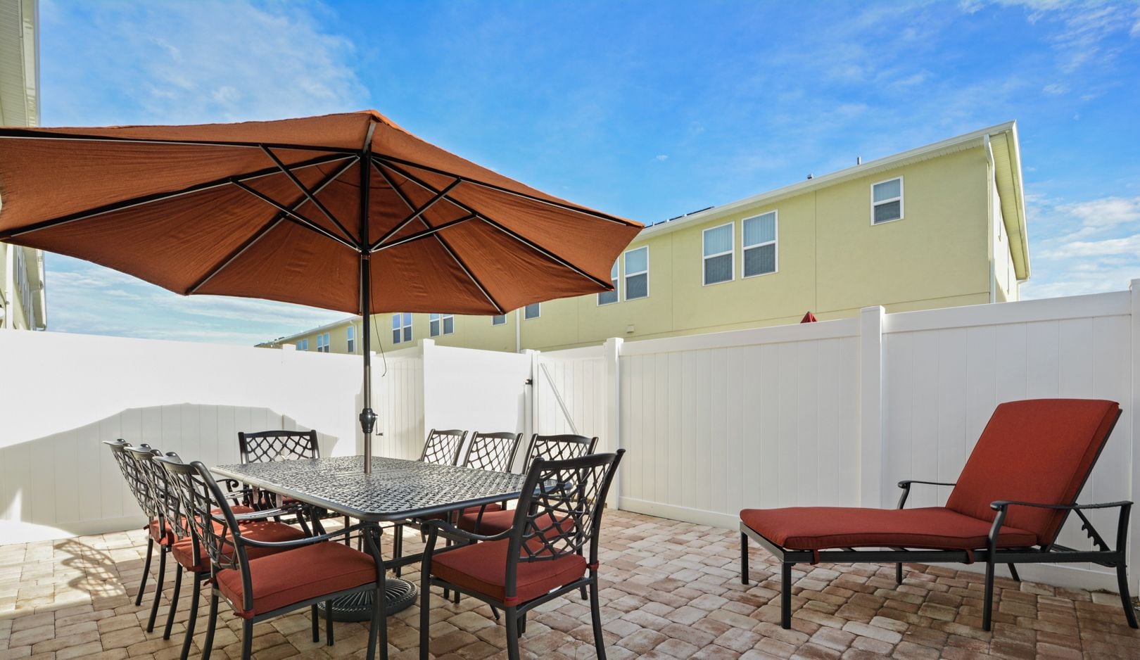 A patio with a table and chairs, a large umbrella, and a white fence.