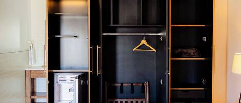 A hotel room with a bed, a wardrobe with multiple compartments, a small table, and a hanging garment rack.