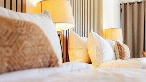 A neatly made bed with white and beige bedding, two bedside lamps, and a striped wall in the background. - Angoria Hotel (San Angelo)