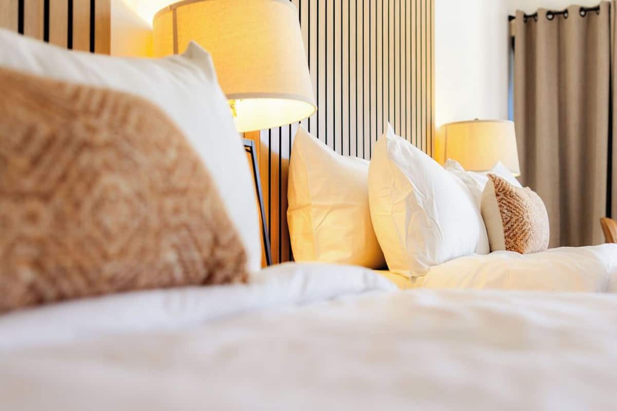 A neatly made bed with white and beige bedding, two bedside lamps, and a striped wall in the background.