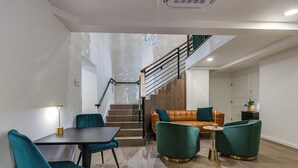 A modern living room with a staircase, teal chairs, a brown leather sofa, and a small side table. - Angoria Hotel (San Angelo)