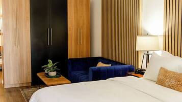 Een hotelkamer met een groot bed, een blauwe bank, een houten garderobe en een nachtkastje met een lamp.