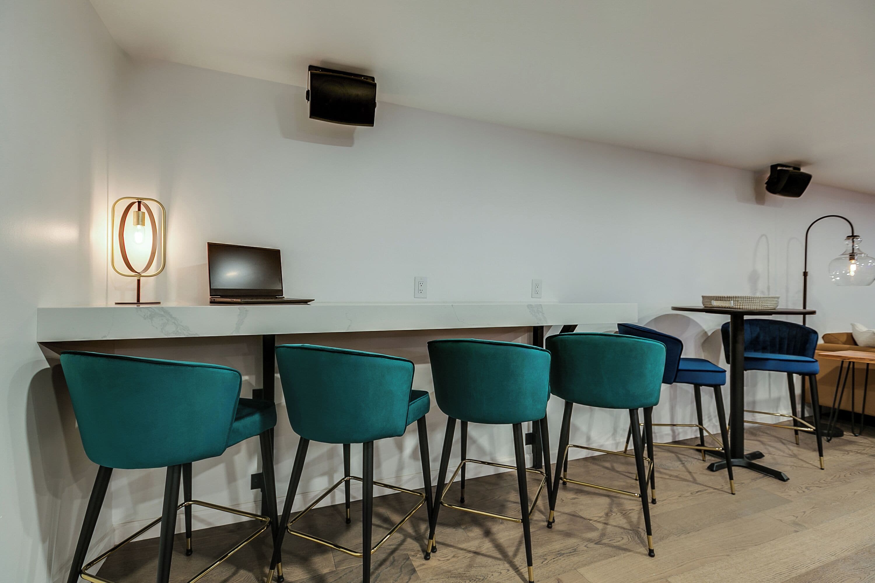 Une cuisine moderne avec un plan de travail blanc, des tabourets de bar turquoise et un luminaire suspendu noir.
