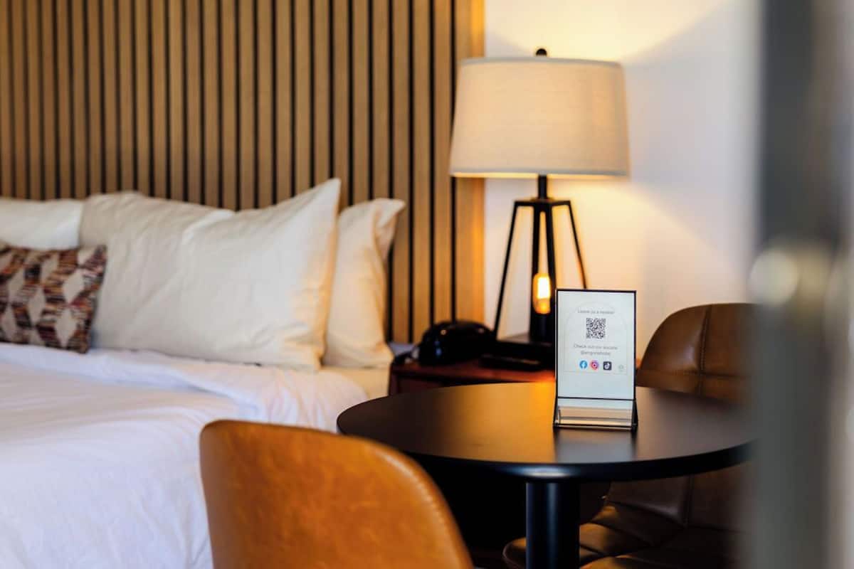 A hotel room with a bed, a desk with a lamp, and a chair.