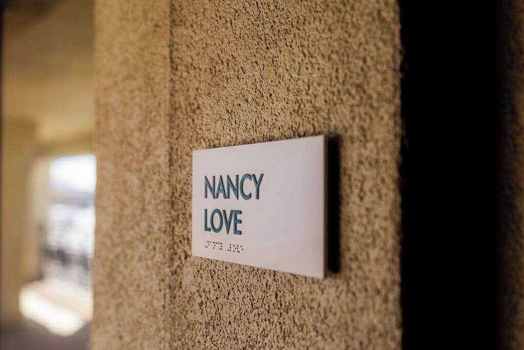A sign on a textured wall with the name "NANCY LOVE" and a phone number.