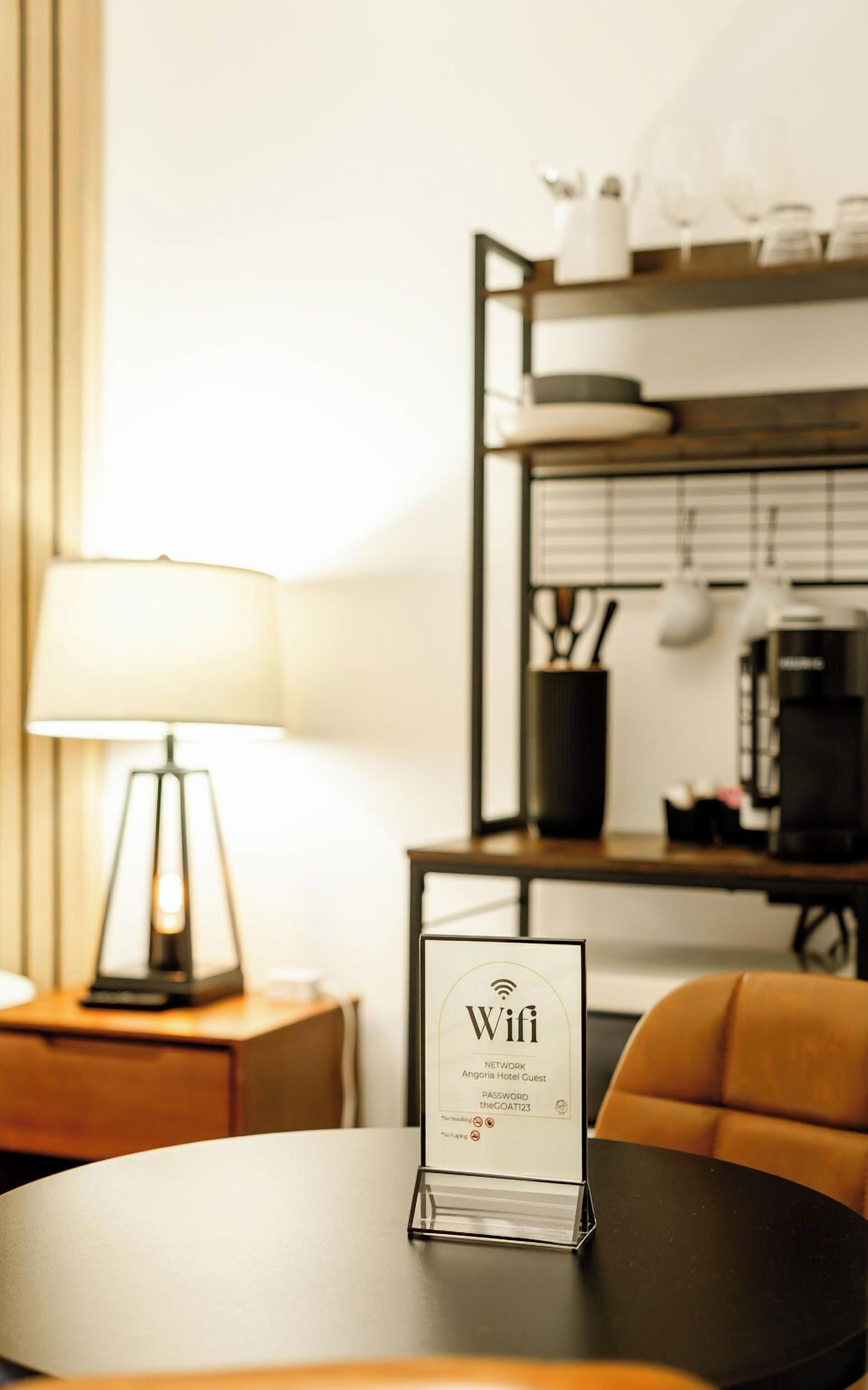 Een hotelkamer met een ronde tafel, een lamp, een bordje dat wifi aangeeft en een koffiezetapparaat.
