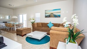 A modern living room with a brown sofa, a white coffee table, and a dining area with a table and chairs.
