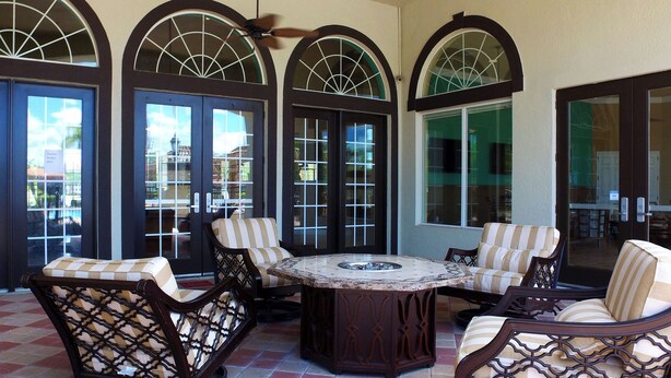 A patio area with a round table surrounded by four cushioned chairs, large arched windows, and a tiled floor.