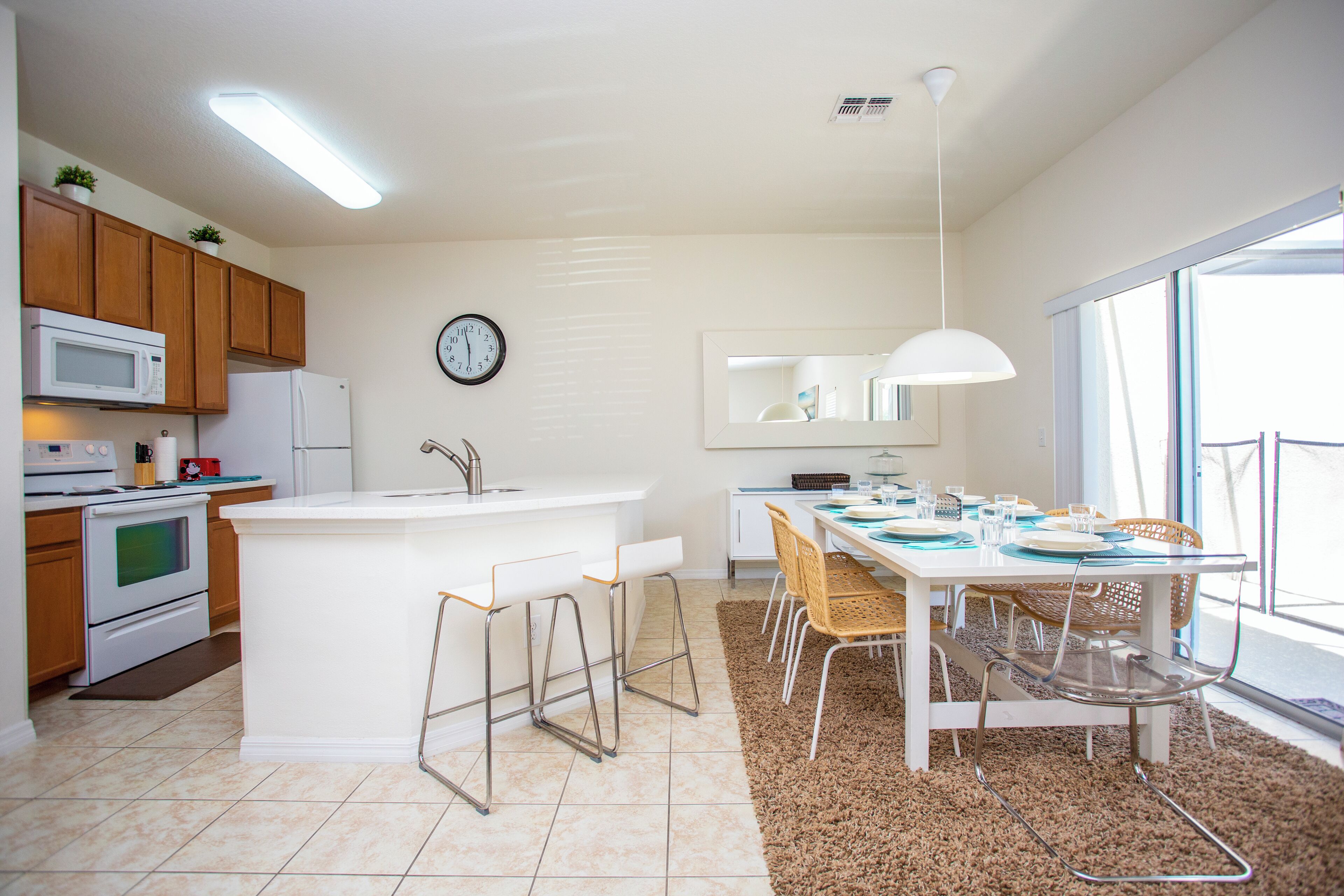 A modern kitchen with wooden cabinets, a white island with bar stools, a microwave, and a refrigerator.